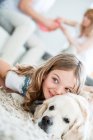 Kleines Mädchen kuschelt mit Hund, liegt auf dem Boden, Eltern zu Hause im Hintergrund — Stockfoto
