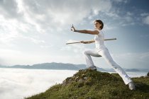 Áustria, Kranzhorn, Mulher adulta média se exercitando com vara de combate no topo da montanha — Fotografia de Stock