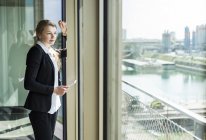 Young businesswoman with digital tablet looking out of window — Stock Photo
