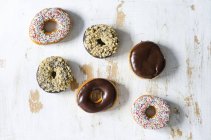 Six different doughnuts with icing and sprinkles on white shabby wood — Stock Photo