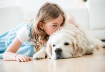 Kleines Mädchen kuschelt mit ihrem Hund, der auf dem Boden liegt — Stockfoto