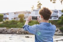 Grecia, Rodas, joven fotografiando con smartphone en primera línea de mar - foto de stock
