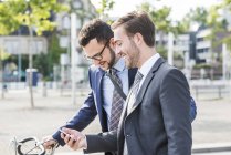 Dois jovens empresários caminhando na cidade, olhando para o telefone celular — Fotografia de Stock
