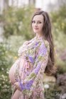 Portrait of pregnant woman wearing fashionable bathrobe holding her belly — Stock Photo