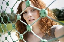 Portrait of redheaded teenage girl looking through net — Stock Photo