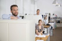Усміхнений чоловік в офісі з колегами на задньому плані — стокове фото