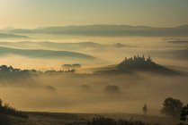 Italien, Toskana, San Quirico d 'orcia, Blick auf hügelige Landschaft bei Sonnenaufgang im Nebel — Stockfoto