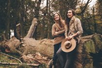 Dos amigas apoyadas en el tronco de un árbol en un parque otoñal - foto de stock