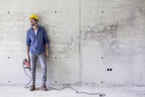Sorrindo homem com chapéu duro no canteiro de obras segurando broca — Fotografia de Stock