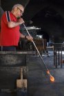 Man blowing with a tube molten glass in a glass factory — Stock Photo