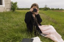 Frau sitzt auf einer Wiese und fotografiert Betrachter — Stockfoto