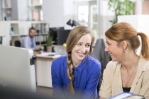Две улыбающиеся женщины в офисе смотрят друг на друга — стоковое фото