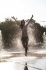 Mulher correndo através da fonte salpicando gotas de água — Fotografia de Stock