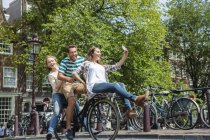 Holanda, Amsterdã, três amigos brincalhões andando de bicicleta na cidade — Fotografia de Stock