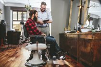 Barbier avec client utilisant une tablette numérique dans le salon de coiffure — Photo de stock
