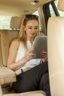 Donna bionda seduta sul sedile posteriore di un'auto con tablet digitale — Foto stock