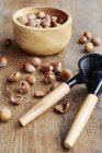 Bowl of hazelnuts, cracked hazelnuts and nut cracker on dark wood — Stock Photo