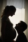 Schwangere und Mann stehen am hellen Fenster — Stockfoto