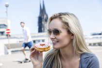 Germany, Cologne, portrait of young woman eating bagel — Stock Photo