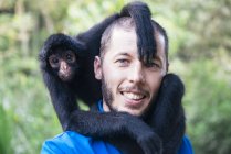 Bolivia, Coroico, portrait of smiling man with black spider monkey on shoulders — Stock Photo