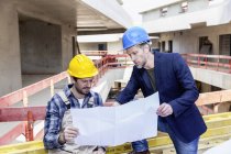 Construction worker and architect with plan talking on construction site — Stock Photo