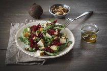 Plate of beetroot salad with rocket and walnuts on wooden surface — Stock Photo