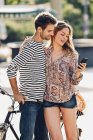Giovani amanti con la bicicletta in piedi per strada guardando lo smartphone — Foto stock