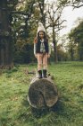 Menina vestindo boné de pé em um tronco de árvore no parque outonal — Fotografia de Stock
