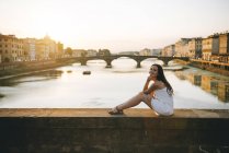 Italia, Firenze, donna felice seduta su un ponte al tramonto — Foto stock