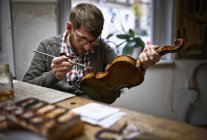 Violin maker in his workshop varnishing repaired violin — Stock Photo