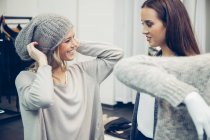 Young woman assisted by friend putting on woolly hat in a boutique — Stock Photo
