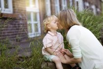 Мама целует своего маленького сына перед домом — стоковое фото