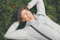 Retrato de un joven sonriente acostado en un prado con las manos detrás de la cabeza - foto de stock