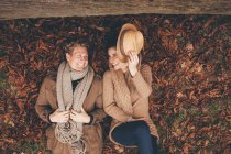 Giovane coppia sdraiata fianco a fianco su foglie autunnali in un parco — Foto stock