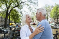Netherlands, Amsterdam, happy senior couple embracing at town canal — Stock Photo