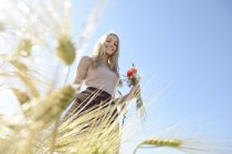 Mujer joven sonriente con ramo de flores de campo de pie en un campo de centeno - foto de stock