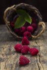 Fresh Raspberries with upturned basket on dark wood — Stock Photo