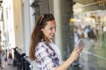 Mujer joven en la ciudad mirando el teléfono celular - foto de stock
