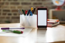 Smartphone su tavolo in legno con penne colorate in camera dei bambini — Foto stock