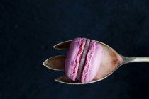 Macaron rosa con cuchara de plata delante de fondo negro - foto de stock