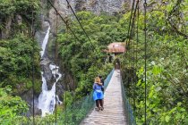 Ecuador, Tungurahua, Banos de Agua Santa, turistas de pie en puente cerca de cascada Pailon del Diablo - foto de stock