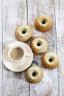 Five mini Gugelhupf cakes with poppy seeds and cup of coffee on wood — Stock Photo