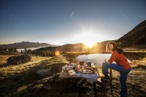 Áustria, Estado de Salzburgo, Altenmarkt-Zauchensee, mulher ao lado da mesa de pequenos-almoços ao nascer do sol — Fotografia de Stock