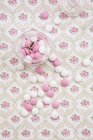Glas aus rosa und weißen Schokoladenknöpfen auf blumig gemustertem Stoff — Stockfoto