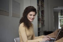 Sorrindo jovem mulher usando laptop no escritório em casa — Fotografia de Stock