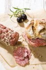 Salami and bread roll on baking paper on table — Stock Photo
