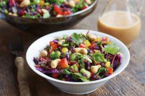 Asian slaw salad with red cabbage, kale, beans, cashew and cilantro in clay bowl and plate on wooden background — Stock Photo