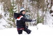 Счастливый мальчик играет со снегом в лесу — стоковое фото