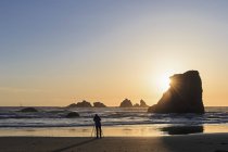 USA, Oregon, Bandon, Bandon Beach, Rocky needles at sunset, female fotographer at beach — Stock Photo