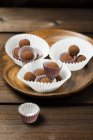 Chocolate truffles in paper cups on wooden platter — Stock Photo